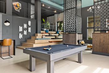 A pool table is in the middle of a room with a chair and a plant.